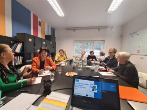 View of a long conference table, people around it, apparently in discussion amongst themselves. In the foreground, there is a notebook computer with an open slideshow identifying the meeting as part of the ISI project.